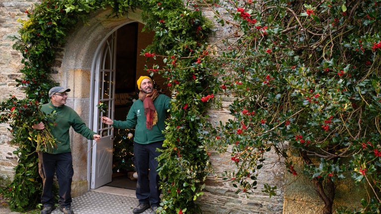 Two gardeners decorate a arbour around the entrance door of the Abbey with green foliage and holly berries